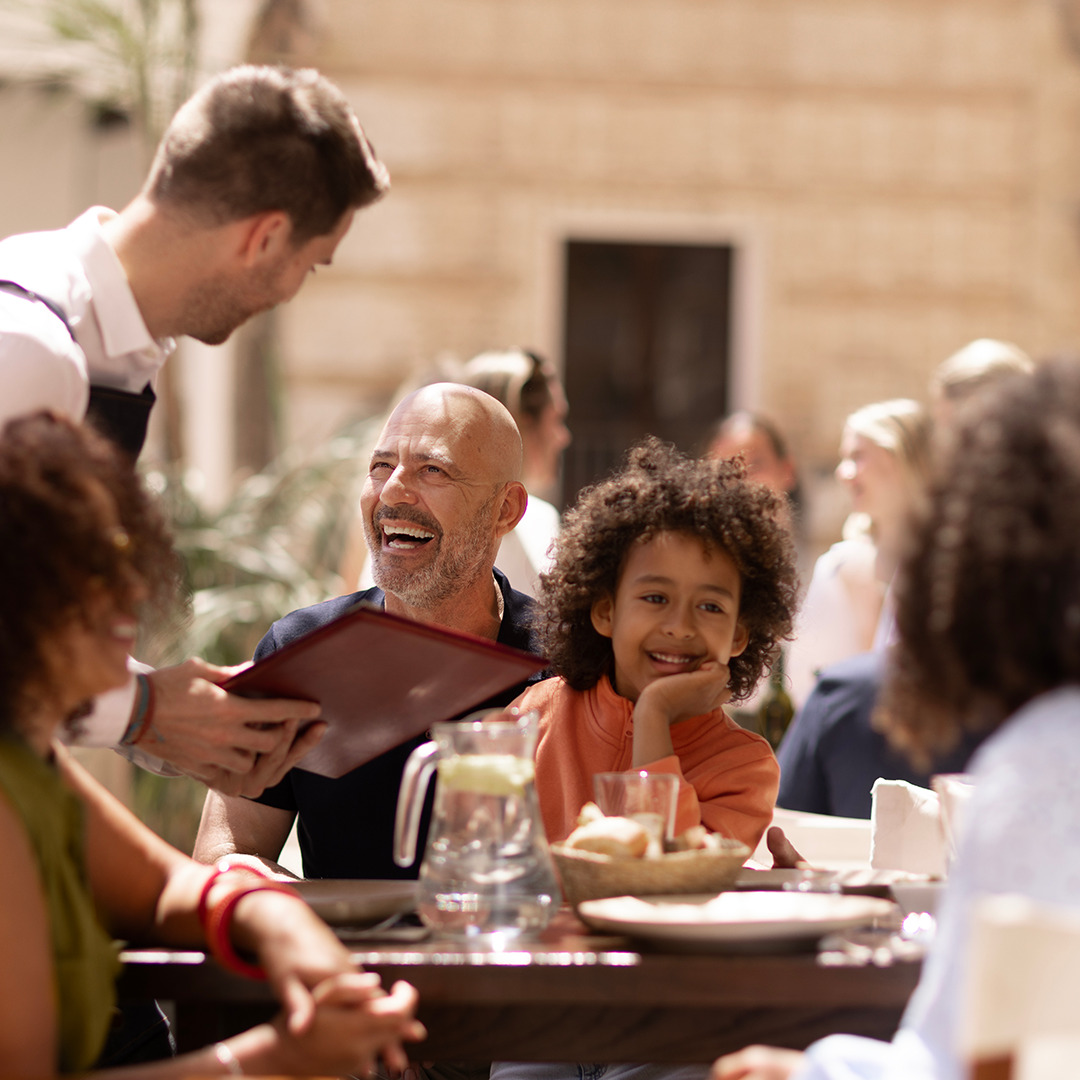 Older man dining outdoors with a child on his knee on a sunny day